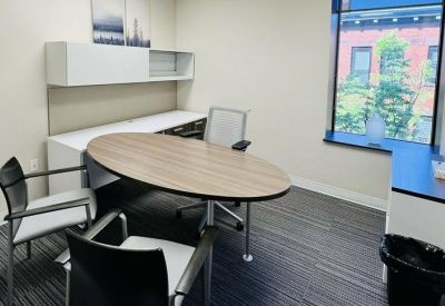 Private office suite with an oval wooden desk, white storage cabinets and window views.