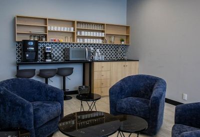 Kitchenette and breakout area with blue velvet armchairs and a patterned backsplash.