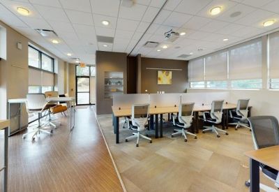 Bright coworking space featuring long wooden desks and ergonomic chairs under a tiled ceiling.