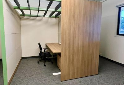 Private wood-panelled workspace booth with a green metal frame and black ergonomic chair.