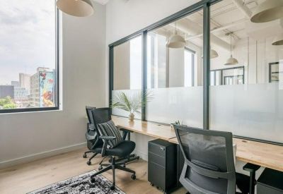 Bright shared office space with wooden desks, ergonomic chairs, and large windows.
