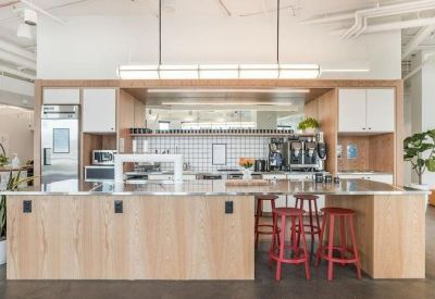 Modern kitchen and breakout area with light wood cabinetry and red bar stools.