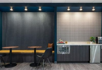 Communal break area with a yellow cushioned bench, small cafe tables, and a kitchen unit with a microwave.