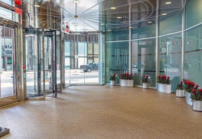 Bright lobby area with polished floors, glass walls, and planters with red flowers near the entrance.