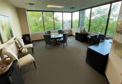 Bright corner office suite featuring a round meeting table, black desk, and large wrap-around windows.