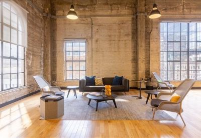 Bright communal lounge with a grey sofa, armchairs, and large arched windows.