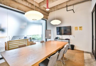 Bright boardroom with a wooden table, grey chairs, and a wall-mounted TV.