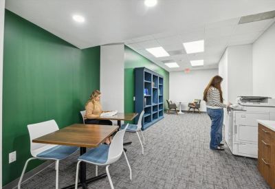 Workroom with a green accent wall, shared tables, and a large copier station.