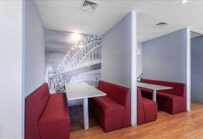 Communal breakout area with red booth seating, white tables, and a monochrome bridge mural.