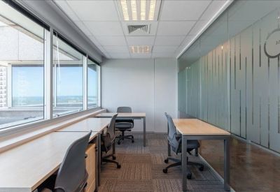 Bright shared office space with a row of desks along floor-to-ceiling windows.