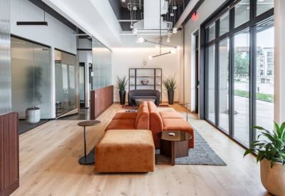 Bright lobby area with orange modular sofas, wooden floors, and floor-to-ceiling windows.