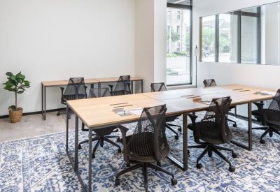 Modern open-plan coworking space with several wooden desks and ergonomic chairs on a patterned rug.