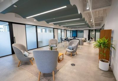 Sunlit lounge area with comfortable grey armchairs and acoustic ceiling baffles.