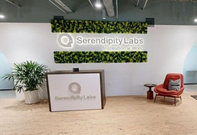 Modern reception area with a branded desk, plush red armchair, and green moss wall features.
