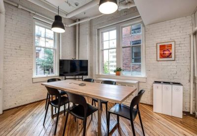 Small meeting room with a wooden table, black chairs, and white brick walls.