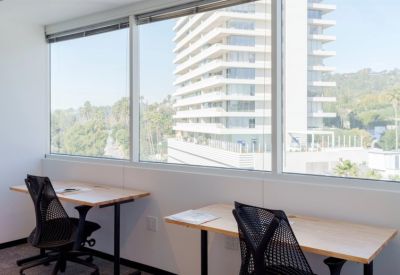 Bright workspace featuring two wooden desks and ergonomic chairs overlooking a city skyline.