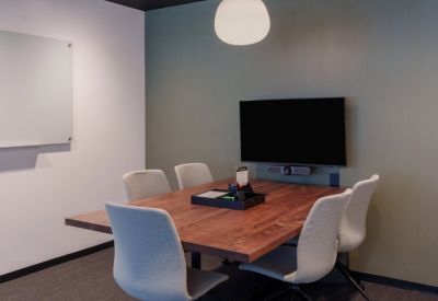 Modern meeting room with a dark wood table, grey upholstered chairs, and a wall-mounted screen.