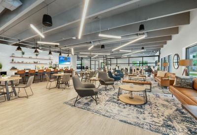 Spacious communal lounge and cafe area with diverse seating, plants, and warm wooden floors.