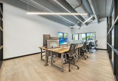Open-plan workspace with industrial ceilings and rows of wooden desks with ergonomic chairs.