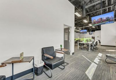 Modern lobby area with black armchairs, side tables, and flat-screen monitors mounted on the wall.
