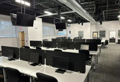 Large open-plan office featuring rows of white desks with dual-monitor setups and black ergonomic chairs.