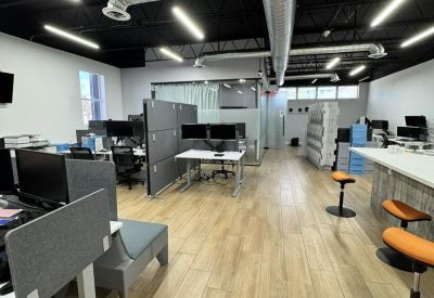 Bright workspace featuring several desks, high-top seating, and industrial ceiling details.