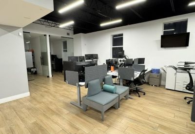 Office lounge area with grey modular seating and a whiteboard under industrial light fixtures.