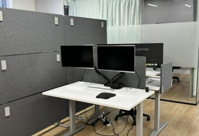 Modern workstation with dual monitors and height-adjustable desk against acoustic paneling.