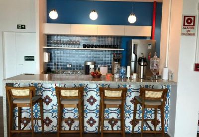 Modern communal kitchen area featuring a tiled bar counter, wooden stools, and blue accent wall.