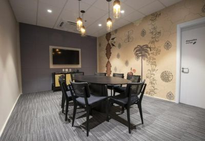 Small meeting room with an oval black table, patterned wallpaper, and hanging designer light bulbs.
