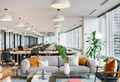 Bright open-plan office featuring grey sofas and rows of desks near large windows.