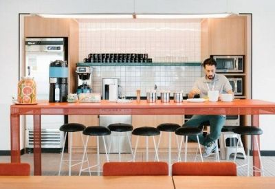 Modern office pantry with a vibrant red high-top table and coffee station.