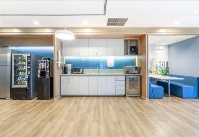 Bright office kitchen and break area with white cabinetry, coffee machine, and blue booth seating.