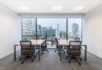 Shared workspace with four desks and ergonomic chairs facing a large window with city views.