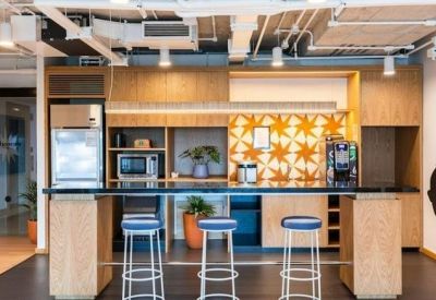 Modern office kitchen featuring a breakfast bar, stools, and patterned backsplash.