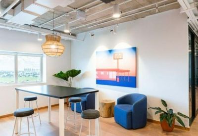 Bright breakout space with a high table, blue armchairs, and colorful wall art.
