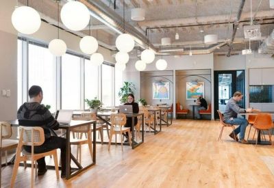 Sunlit coworking area with wooden floors and round pendant lighting above several shared desks.