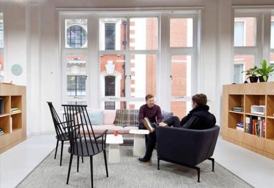Meeting area with a grey rug, designer chairs, and large windows.