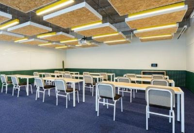 Training room with rows of white desks and grey chairs against a green paneled wall.