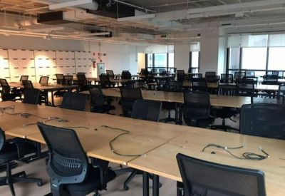 Large open-plan office space with rows of light wood desks and ergonomic black mesh chairs.
