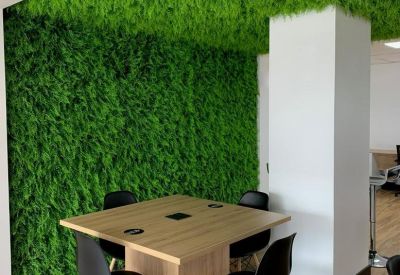 Modern meeting area with a light wood table and a large green moss-covered wall and ceiling.