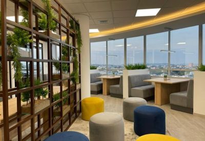 Communal lounge with grey booths, colorful stools, and a wooden room divider with plants.