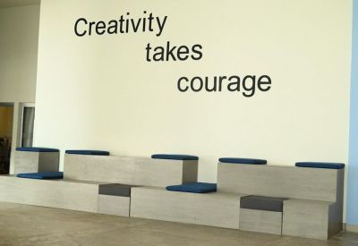 Waiting area with modern tiered wooden seating and a feature wall reading Creativity takes courage.