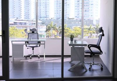 Glass-walled office suite featuring two desks and views of urban high-rises through large windows.
