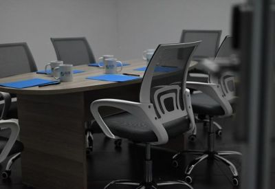 Close-up of a modern meeting room with grey mesh chairs and blue folders on a wooden table.