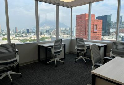 Open-plan workspace with multiple desks and floor-to-ceiling windows showing city views.