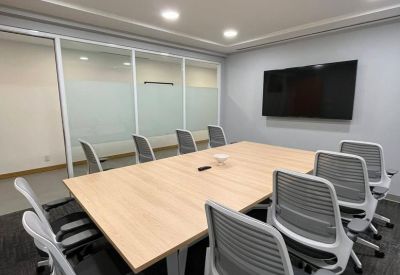 Professional meeting room with a light wood table, grey mesh chairs, and a wall-mounted TV.