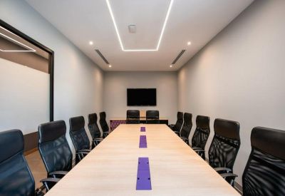 Boardroom with a long wooden table and black ergonomic chairs under bright panel lighting.
