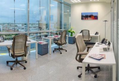 Bright office space with white desks and ergonomic mesh chairs near large windows.