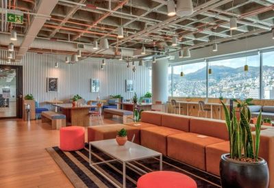 Spacious communal lounge with orange sofas, coffee tables, and panoramic city views through large windows.